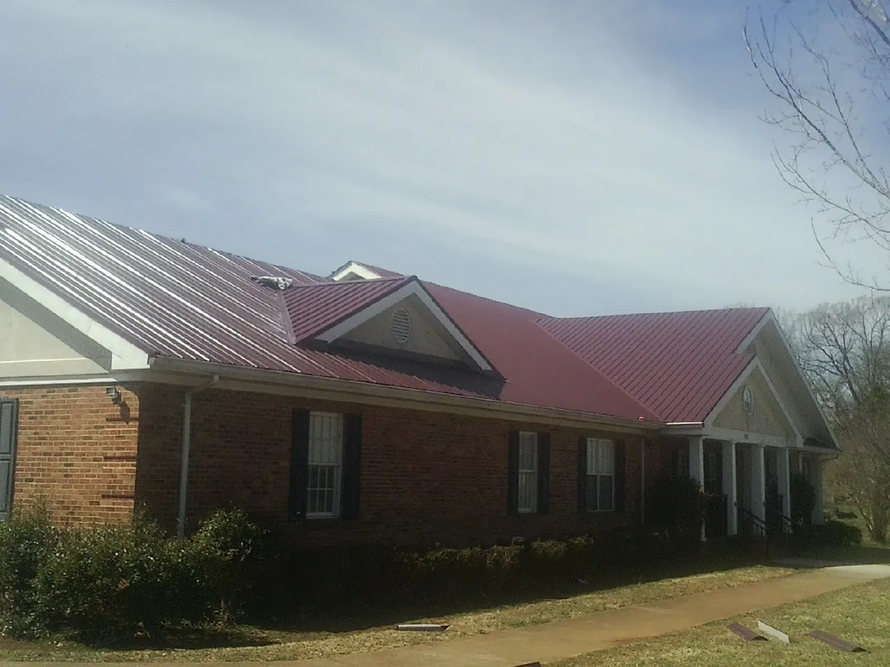 Red metal roof with gabled entries on a long brick building, from a Hail Damage Roof Repair job in Taos