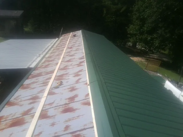 Old rusted panels beside newly installed green metal roofing — Wind Damage Roof Repair by Roofing Brothers in Taos
