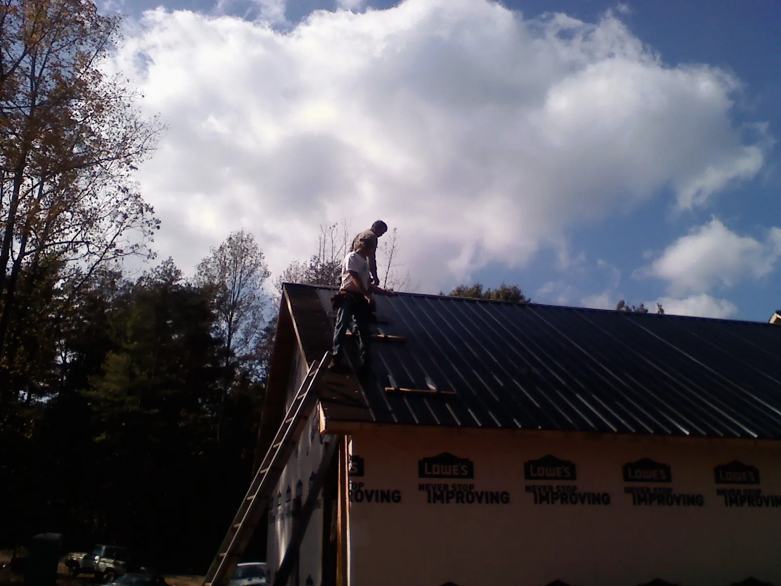 Roofer fastening dark metal panels high against a cloudy sky, from a Roof Inspection job in Taos