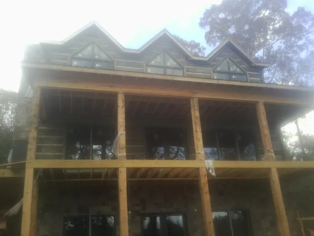 Dormers and porch framing on a large log home under construction — Roof Coating work by our crew in Taos