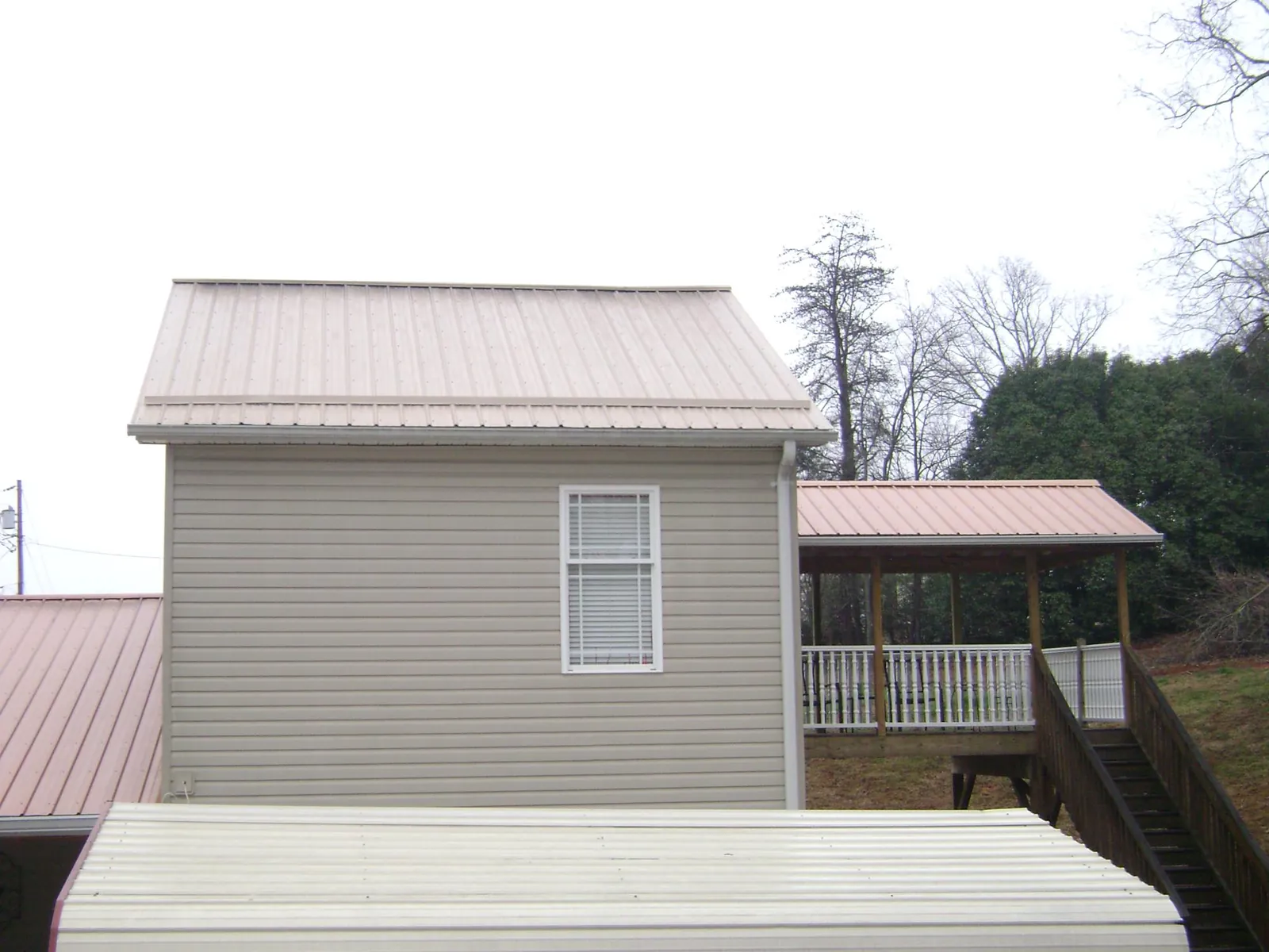Tan metal roofs on a two story addition and attached porch, from a Roof Replacement job in Taos