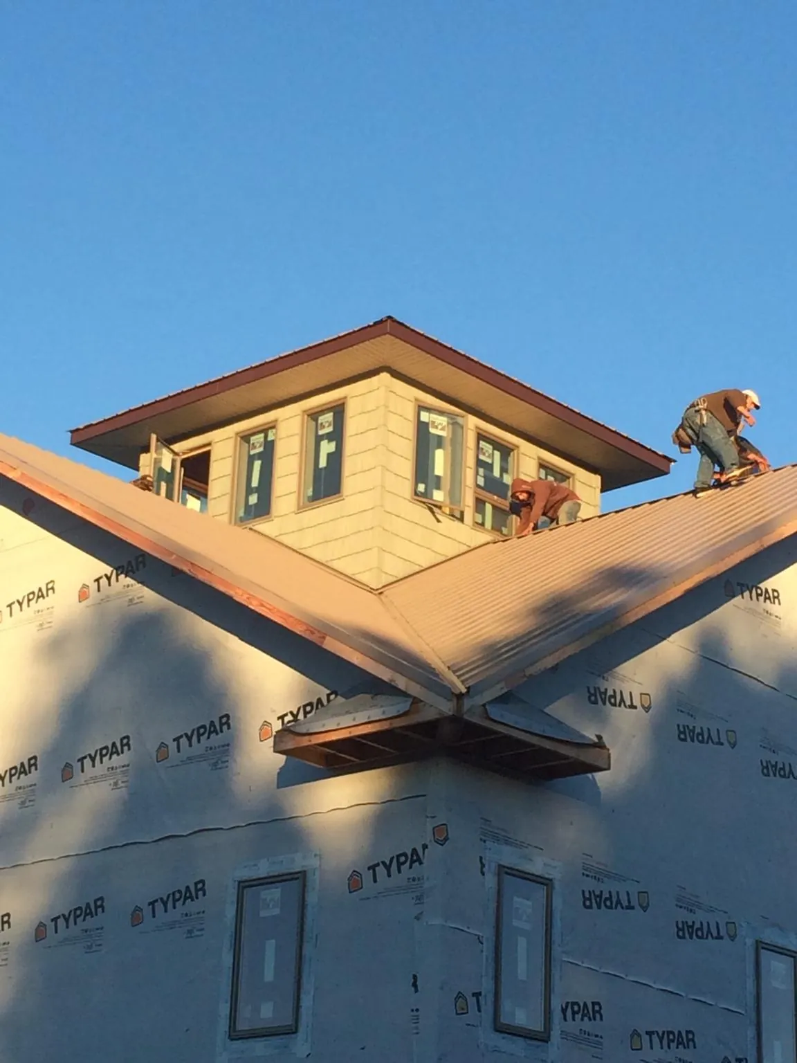 Roofers working around a rooftop cupola on a new metal roof at sunset in Taos